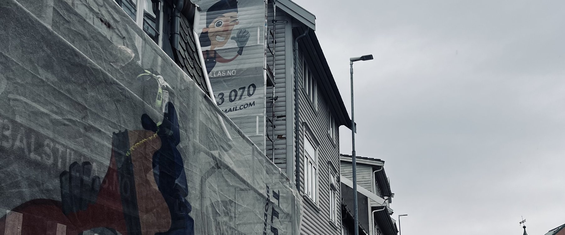 Stillasduk med Brødrene Rajchelt-maskoten, telefonnummer og e-post på fasade i Tromsø sentrum